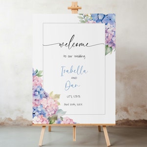 Peut inclure: Une pancarte de bienvenue de mariage avec des hortensias aquarellés dans des tons de bleu et de rose. La pancarte indique "Bienvenue à notre mariage Isabella et Dan Ville, État 29 avril 202X".