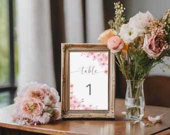 May include: A gold-framed table number card with a watercolor design of pink flowers. The card reads "Table 1".