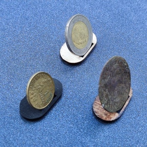 Puede incluir: Tres soportes de madera para monedas con diferentes monedas en la parte superior. Los soportes están hechos de madera y tienen un diseño simple. Las monedas son de diferentes tamaños y colores.