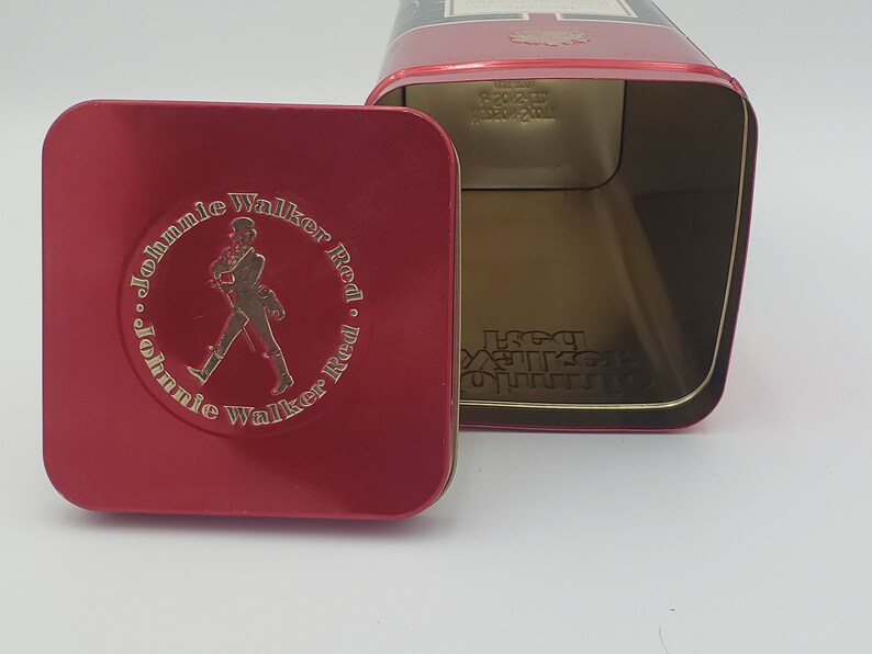 K&ouml;nnte beinhalten: Rote Blechdose mit einem Johnnie Walker Red Label Logo. Die Dose ist ge&ouml;ffnet und der Innenraum ist leer.