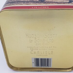 K&ouml;nnte beinhalten: Goldene Metalldose mit einem roten Band und einem gedruckten Bild einer Jagdszene. Die Dose ist mit "1.75 LITRES", "HUDSON SCOTT & SONS-LTD", "EST. 1901", "MANUFACTURERS OF TIN BOXES SINCE 1901", "CARLISLE ENGLAND" beschriftet und hat einen Barcode mit der Nummer "0 88508 02050".