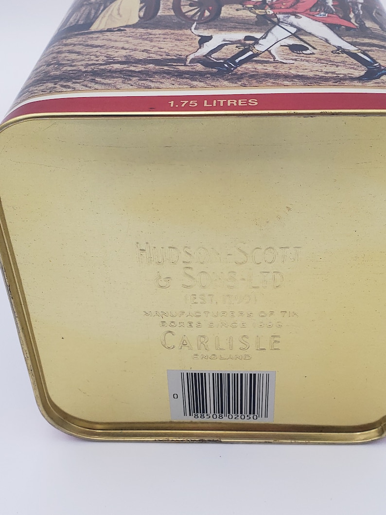 K&ouml;nnte beinhalten: Goldene Metalldose mit einem roten Band und einem gedruckten Bild einer Jagdszene. Die Dose ist mit "1.75 LITRES", "HUDSON SCOTT & SONS-LTD", "EST. 1901", "MANUFACTURERS OF TIN BOXES SINCE 1901", "CARLISLE ENGLAND" beschriftet und hat einen Barcode mit der Nummer "0 88508 02050".