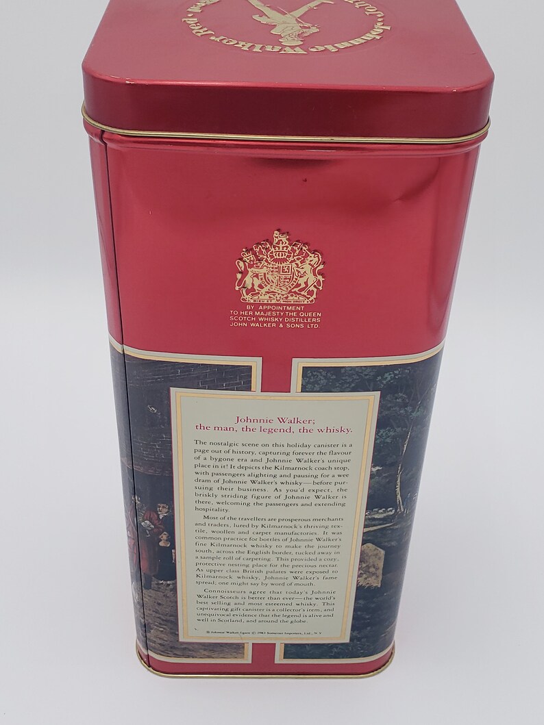 K&ouml;nnte beinhalten: Rote Blechdose mit einer Vintage-Illustration einer Pferdekutsche und Personen vor einem Geb&auml;ude. Der Text auf der Dose lautet "Johnnie Walker: Der Mann, die Legende, der Whisky."