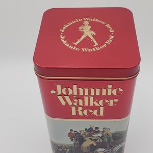 K&ouml;nnte beinhalten: Rote Blechdose mit einem Johnnie Walker Red-Etikett und einer Vintage-Illustration einer Kutsche, die von Pferden gezogen wird. Die Oberseite der Dose hat ein kreisf&ouml;rmiges Logo mit dem Text "Johnnie Walker Red" und einem Mann, der mit einem Stock geht.
