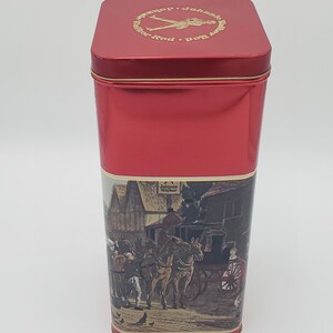 K&ouml;nnte beinhalten: Rote Metalldose mit einem goldenen Etikett, auf dem ein Mann zu sehen ist, der geht, und der Text "Johnnie Walker Red Label". Das Etikett zeigt auch eine Szene mit einer von Pferden gezogenen Kutsche mit Personen vor einem Geb&auml;ude.