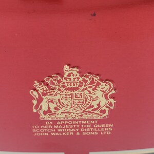 K&ouml;nnte beinhalten: Ein rotes Etikett mit einem goldenen k&ouml;niglichen Wappen und dem Text "By Appointment to Her Majesty The Queen Scotch Whisky Distillers John Walker & Sons Ltd."