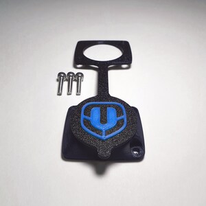 Könnte beinhalten: Eine schwarze Plastikabdeckung mit einem blauen "U"-Logo. Die Abdeckung hat eine runde Öffnung und einen Griff. Drei kleine silberne Schrauben sind im Lieferumfang enthalten.