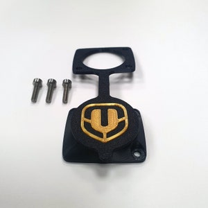 Puede incluir: Pieza de plástico negro impresa en 3D con un logotipo U dorado. La pieza tiene tres agujeros para tornillos y una abertura redonda. Se incluyen tres tornillos plateados.