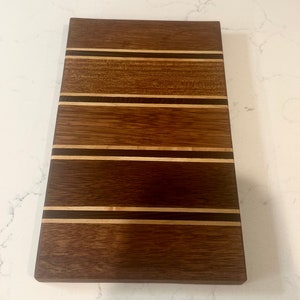 May include: A rectangular wooden chopping board with a striped pattern of light and dark wood. The board is made of walnut and maple wood.