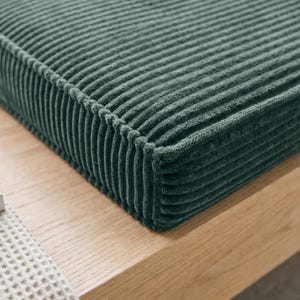 May include: A rectangular cushion featuring a deep forest green corduroy fabric with a distinct vertical ribbed texture. The cushion has structured, piped edges that define its shape, showcasing the soft, plush material and consistent color.