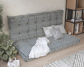 Può includere: Un divano da pavimento rivestito in tessuto pied-de-poule blu navy e bianco con bottoni trapuntati sullo schienale. Il divano include tre cuscini decorativi in tonalità neutre e una coperta bianca testurizzata drappeggiata sulla seduta.