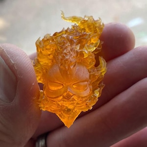 Puede incluir: Una figurita de un cráneo con llamas, impresa en 3D, hecha de resina naranja transparente.