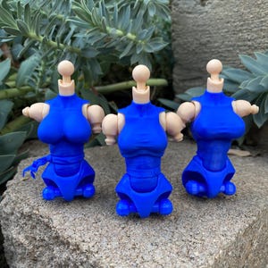 Puede incluir: Tres torsos de figuras de acción de plástico azul con cuellos y hombros articulados en tono de piel claro. Cada torso presenta un corpiño y una sección de cadera azul esculpidos con puntos de articulación visibles en cuello y hombros.