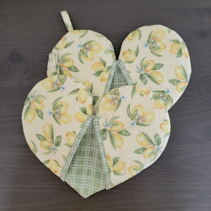 May include: Three heart-shaped lemon-patterned pot holders with a green plaid backing. The pot holders are quilted and have a loop for hanging.