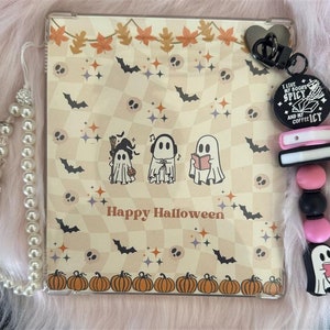 Könnte beinhalten: Eine transparente Handyhülle aus Kunststoff mit Halloween-Motiv. Die Hülle hat einen karierten Hintergrund mit Fledermäusen, Sternen und Totenköpfen. Auf der Hülle sind drei Geister abgebildet, einer mit einem Besen, einer mit Kopfhörern und einer, der ein Buch liest. Der Text "Happy Halloween" ist auf der Hülle aufgedruckt.