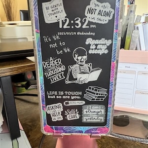 May include: A black phone case with a variety of colorful stickers. The stickers have inspirational quotes and messages, such as "Be Gentle With Yourself", "You Are Not Alone", "Reading Is My Escape", and "Life Is Tough But So Are You".