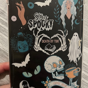 May include: Black phone case with a spooky Halloween theme. It features a skull drinking coffee, a ghost, a bat, a witch, and the text "Stay Spooky" and "Death by TBR".