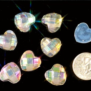 Könnte beinhalten: Eine Gruppe von regenbogenfarbenen herzförmigen Strasssteinen, einige mit einem karierten Muster, sind auf einer schwarzen Oberfläche verstreut. Eine US-amerikanische Viertel-Dollar-Münze dient als Größenvergleich.