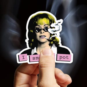 May include: A sticker with a pop art design of a woman wearing pixelated sunglasses and smoking. The sticker includes the text "I sm pot" in pink boxes.
