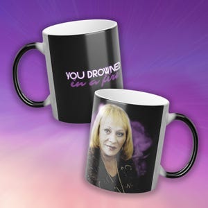 May include: Black and white heat-sensitive mug with a portrait of a woman and the text "YOU DROWNED in a fire" in purple. The mug's handle is black.