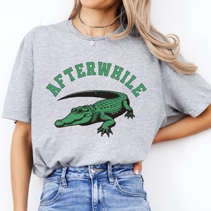 May include: Gray t-shirt with a green alligator graphic and the text "Afterwhile" in a black, white, and green font.