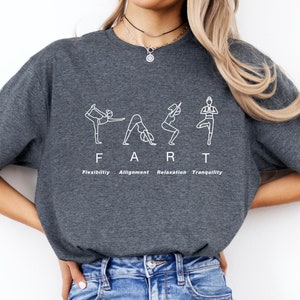 May include: Dark gray t-shirt with white text and yoga poses spelling out "FART". Below the word are the words "Flexibility, Alignment, Relaxation, Tranquility". The shirt is made of a soft material.