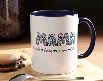 May include: White ceramic mug with a blue rim and handle. The mug has a blue and white floral design that spells out "MAMA" in large letters. Below the letters are the names "Amanda, Brady, Camron, Chloe" with a heart symbol between each name.