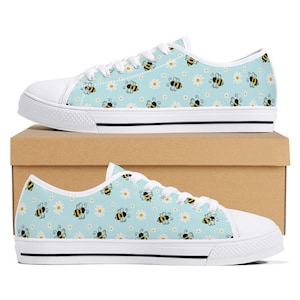 Può includere: Sneakers basse in tela bianca con sfondo blu e un motivo di api gialle e nere e margherite bianche.