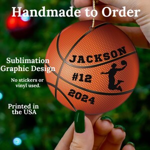 May include: A round basketball ornament with the name "JACKSON", number "12", and the year "2024". The ornament has a sublimation graphic design and is printed in the USA. The text "Handmade to Order" is at the top.