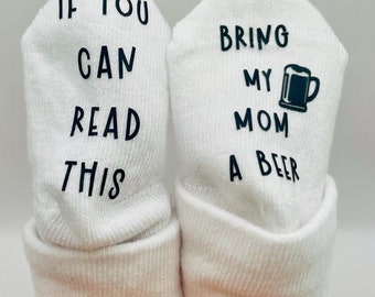 May include: A pair of white baby socks with black text. One sock reads "If you can read this" and the other sock reads "Bring my mom a beer" with a beer mug icon.