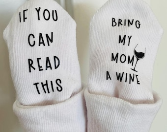 May include: A pair of white baby socks with black text. One sock says "If you can read this" and the other sock says "Bring my mom a wine" with a wine glass icon.