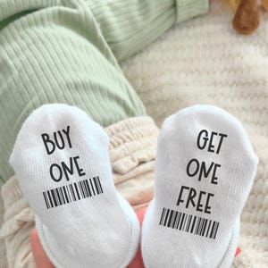 May include: A pair of white baby socks with black text. One sock says "BUY ONE" with a barcode underneath. The other sock says "GET ONE FREE" with a barcode underneath.