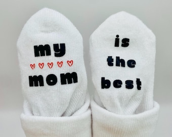 May include: White baby socks with black text that reads "my mom" with red hearts and "is the best" on each sock.