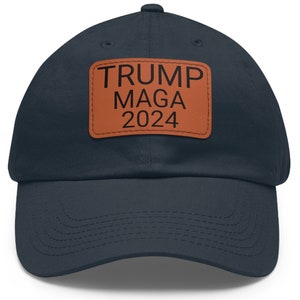Puede incluir: Una gorra de béisbol azul marino con un parche de cuero marrón que dice "TRUMP MAGA 2024".