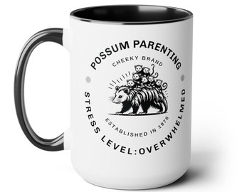 Peut inclure: Une tasse en céramique blanche avec un bord et une poignée noirs. La tasse présente une illustration en noir et blanc d'un opossum avec des bébés sur son dos. Le texte "Possum Parenting Cheeky Brand Stress Level: Overwhelmed Established in 1978" est imprimé autour de l'illustration.