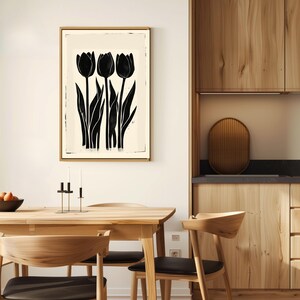 May include: A framed art print featuring a black and white tulip design. The artwork showcases three stylized black tulips with long stems and leaves against a cream-colored background. The frame is a light wood color, and the print is displayed in a dining room setting.