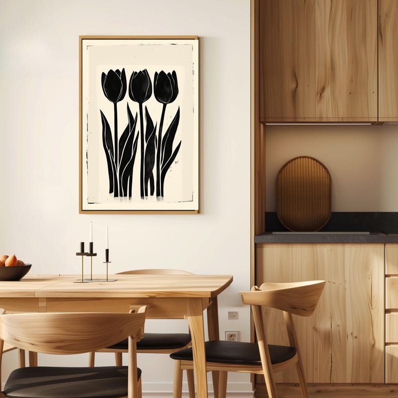 May include: A framed art print featuring a black and white tulip design. The artwork showcases three stylized black tulips with long stems and leaves against a cream-colored background. The frame is a light wood color, and the print is displayed in a dining room setting.