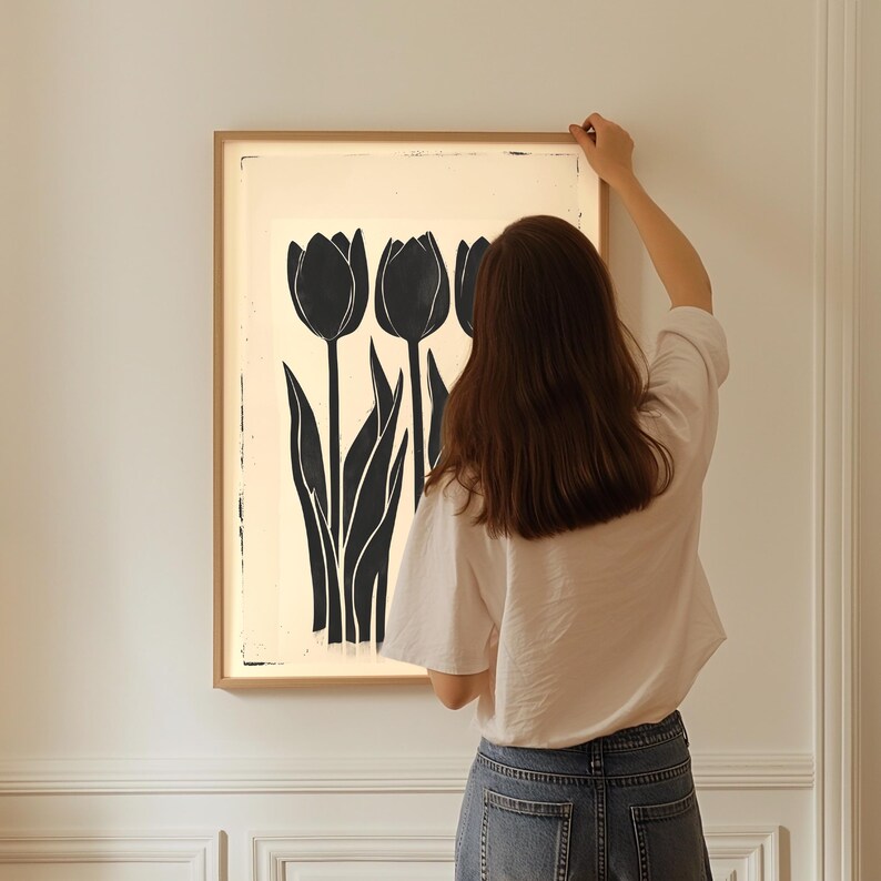 May include: A framed art print featuring a black and white tulip design. The artwork showcases three stylized tulips with long, slender leaves against a cream-colored background. The frame is a light wood color, adding a natural touch to the floral art.