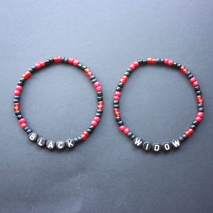 Puede incluir: Dos pulseras de cuentas. Una pulsera deletrea "BLACK" en cuentas de letras blancas, y la otra deletrea "WIDOW". Las pulseras están hechas con cuentas negras, rojas y transparentes.