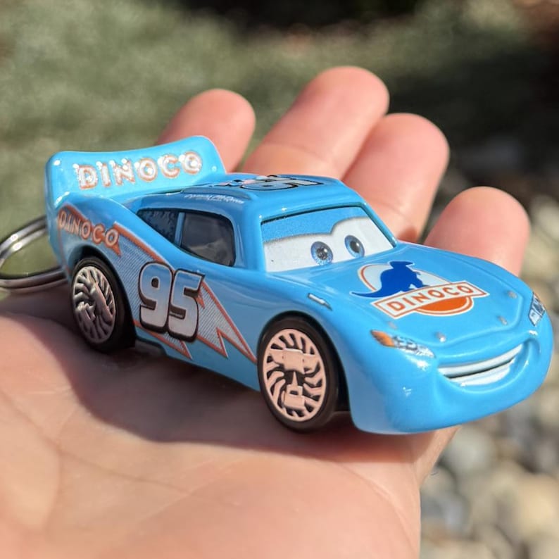 Może przedstawiać: Jasnoniebieski samochodzik z numerem 95 i napisem "Dinoco". Samoch&oacute;d ma wz&oacute;r błyskawicy i spojler. Samoch&oacute;d jest brelokiem.