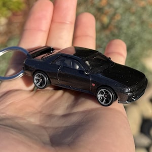 May include: A black die-cast model car keyring. The miniature car features detailed wheels and a spoiler. The keyring is silver. The car is approximately 7.6 cm long.