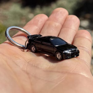 May include: A black die-cast model car keychain with a silver key ring. The miniature car features detailed wheels and a spoiler. The car is a sleek, black color.