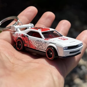 May include: White and red toy car keyring with black wheels. The car has the number 426 and the word MOPAR printed on the side. The car has a spoiler and the word Dodge printed on the front.