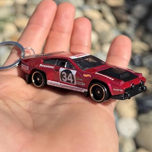 May include: A white ceramic mug with a black handle and the text "But First, Coffee" in a bold, black font. The mug is set against a blurred background, suggesting a cozy setting.