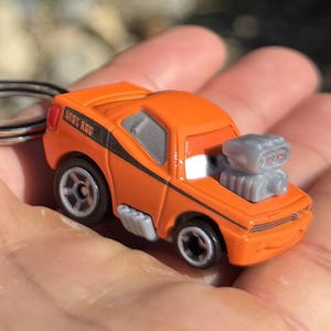 May include: Orange toy car with the text "SHOT ROD" on the side. The car has a gray engine and black wheels. A black stripe runs along the side of the car.