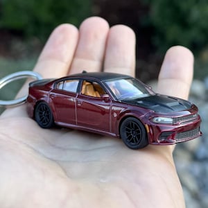 以下が含まれることがあります： 黒い屋根とボンネット、黒いホイールを備えた、ミニチュアのバーガンディ色の車。 車にはキーホルダーが付いています。 インテリアはタン色です。 車は詳細なレプリカです。
