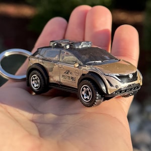 May include: A gold-colored toy car with black accents and a keychain ring. The car has the text "POLE TO POLE" printed on the side. The car has black wheels and a black roof rack.