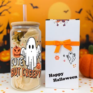 May include: A clear glass tumbler with a bamboo lid and straw, featuring a white ghost, orange pumpkins, and the text "CUTE BUT CREEPY". Beside it is a white rectangular gift box with an orange ribbon, a ghost sticker, and "Happy Halloween" text.