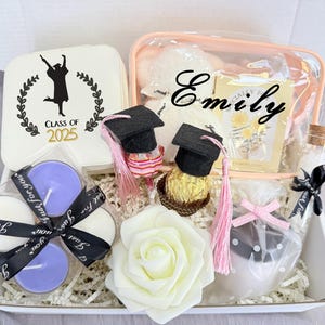 May include: A graduation gift box with a variety of items. Includes a white box with a lid that says "Class of 2025", candles, a clear cosmetic bag, miniature graduation caps, a white rose, and other decorative items.