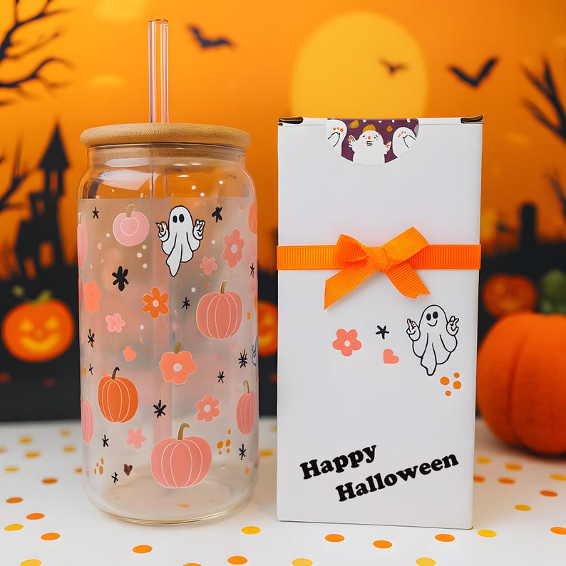 May include: A clear glass tumbler with a bamboo lid and glass straw, featuring a pattern of ghosts, orange pumpkins, and flowers. Beside it stands a white rectangular gift box tied with an orange ribbon, printed with Happy Halloween text.
